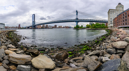 Pebble beach and the Manhattan Bridge with rainy clouds in New York City.