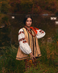 Young woman dressed traditional ukrainian embroidered clothes. Portrait of beautiful confident girl with long dark hair and brown eyes looking at camera outdoors. Vintage outfit.