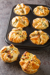 Puff pastry muffins stuffed with spinach and feta cheese close-up in a muffin pan on the table....