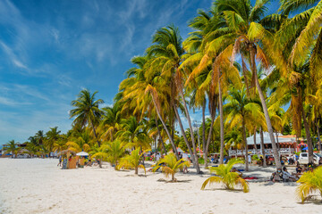 People are sunbathing in the shadow of cocos palms on white sand beach, Isla Mujeres island,...