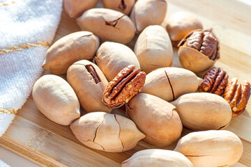 Many brown pecan nuts on light wooden background close up.