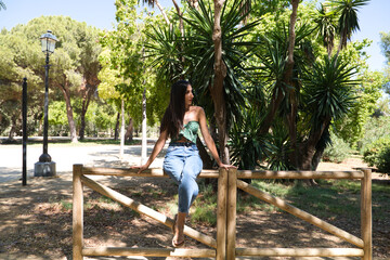 Beautiful woman with black hair leaning on a wooden railing in the park. The woman is doing...