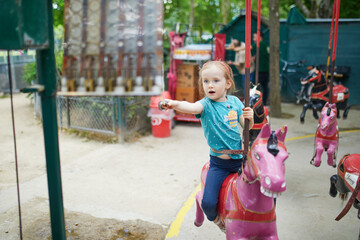 Adorable preschooler girl on a horse of traditional Parisian vintage merry-go-round where children...