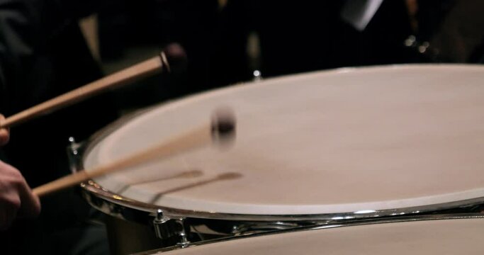 Close up slow motion shot of a timpani player during a concert to classical music drumming fast with the drumsticks to mozart requiem
