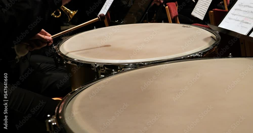 Poster close up handheld shot of a timpani player during a concert with an orchestra with view of other ins