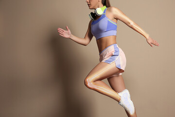 Digital composite of highlighted bones and woman in sportswear with headphones running on beige background