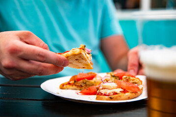 man Hand takes a slice of pita Pizza with Mozzarella cheese, ham, bacon, tomato, Spices in outdoor cafe