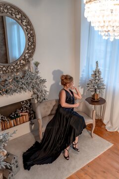 Portrait of a wealthy mature woman with evening make-up and hairstyle posing in a black dress on the background of the Christmas room. Luxurious lifestyle. Christmas holidays concept