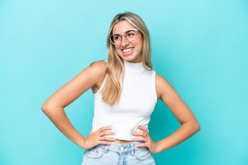 Young caucasian woman isolated on blue background posing with arms at hip and smiling