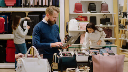 In a big accessories shop supervisor man using laptop to verify the stuff from the stores while...