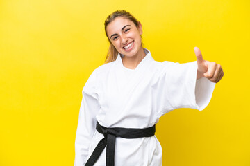 Young caucasian woman doing karate isolated on yellow background giving a thumbs up gesture © luismolinero