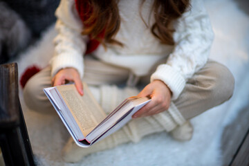 A girl with a book is sitting on the floor on a furry white carpet. Dressed in a white sweater and...