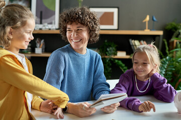 Happy mother laughing together with her children while they sitting at table and reading book
