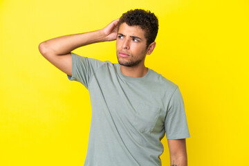 Fototapeta na wymiar Young handsome Brazilian man isolated on yellow background having doubts while scratching head
