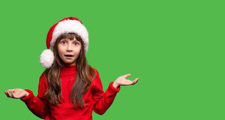 Disappointment gesture. The girl in the Santa hat opened her mouth and opened her arms in different directions. Emotional portrait of a child. Expectation and reality did not match. No gifts