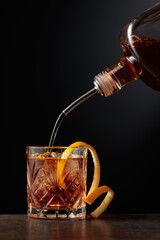 Whiskey is poured into a glass with ice and orange peel. - obrazy, fototapety, plakaty