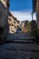 Tourist woman climbing from below a beautiful street with stairs of a medieval old town in Catalonia in Rupit with lights and shadows
