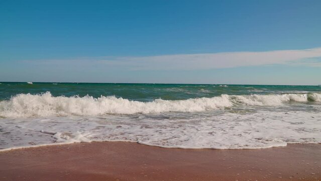 Wind raises white waves on sea. Sea, waves on beach in summertime against blue sky, slow motion. Travel concept, Landscapes overlooking beach sea sand and blue sky. Ocean, breeze drives wave to beach