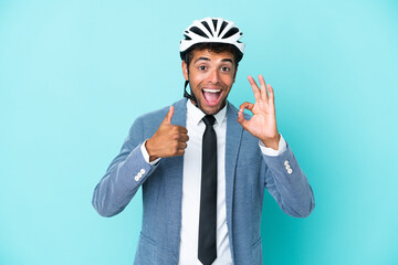 Young business Brazilian man with bike helmet isolated on blue background showing ok sign and thumb up gesture