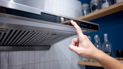 Male hand turn on extractor fan of cooker hood in the kitchen. Modern home appliance for cooking lifestyle.