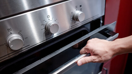 Male hand opening oven door in the kitchen showroom. Buying cooking appliance for domestic kitchen....
