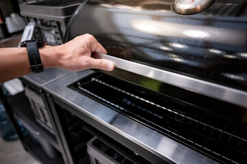 Male hand opening outdoor gas barbecue (BBQ) grill in the kitchen showroom. Buying cooking...