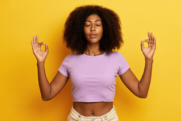 Portrait of relaxed dark skinned young lady with fluffy hair, makes meditation with closed eyes and...