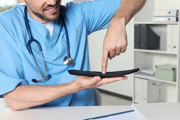Male orthopedist showing insole in hospital, closeup