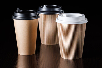 Several disposable paper cups with lids of different types and sizes for drinks on a black background. Side view.