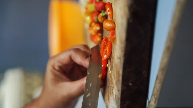 vertical video of a woman's hand slicing a red chili with a kitchen knife