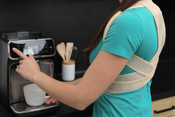 Woman with orthopedic corset making cup of coffee indoors, closeup