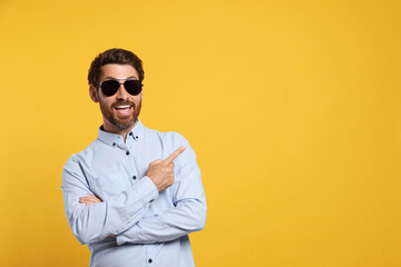 Fototapeta premium Portrait of excited bearded man with stylish sunglasses on orange background. Space for text