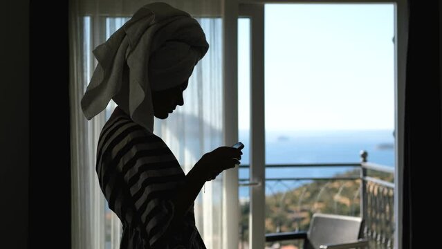 silhouette of a woman with a phone on the background of a window overlooking the sea