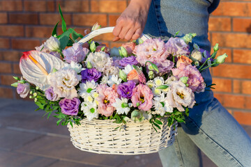 Woman walking and holding big and beautiful wicker basket with fresh roses, eustoma and other flowers