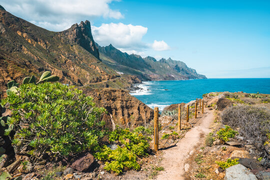 Landscape with picturesque pathway through the rocky landscape and ridges of mountain peaks. Blue Atlantic ocean waves foaming. Tenerife, Anaga National park. Unesco heritage. Roque de las Animas.