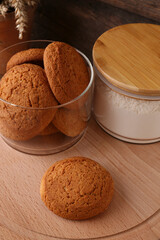 Cookies and jar of wheat flour on wooden board, closeup view