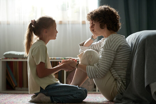 Little girl sitting on floor with her mom and holding her hand, she supporting her in her problems