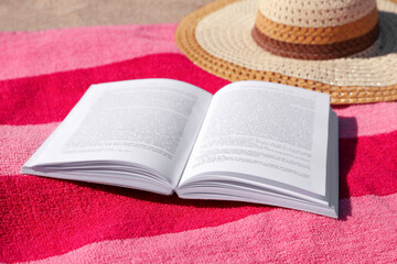 Open book, hat and striped towel on sandy beach