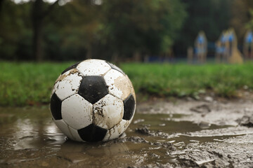 Fototapeta na wymiar Dirty leather soccer ball in puddle outdoors