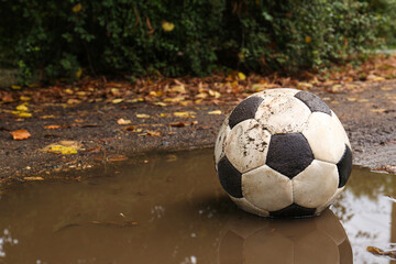 Dirty soccer ball in muddy puddle, space for text