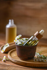 Bottle of chamomile essential oil and flowers on wooden table