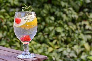 Delicious refreshing lemonade with raspberries on wooden table outdoors, space for text