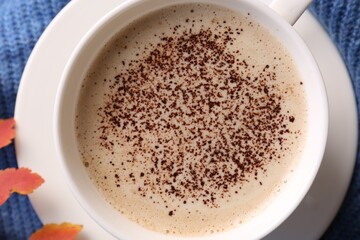 Cup of hot drink and leaves on blue knitted fabric, top view. Cozy autumn atmosphere