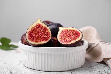 Bowl of tasty ripe figs on white textured table, closeup