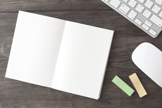 Blank notebook, keyboard and white mouse on a dark wooden desk	