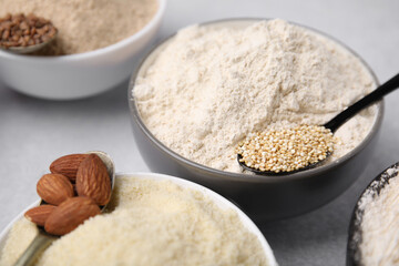Bowls with different types of flour and ingredients on light grey table, closeup