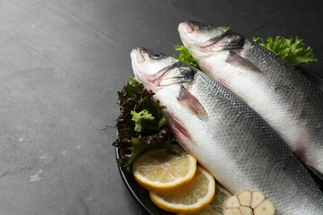 Fresh raw sea bass fish and ingredients on black table, space for text