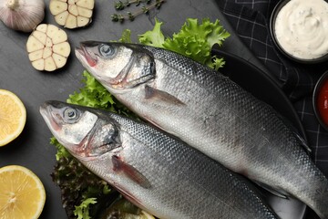 Fresh raw sea bass fish and ingredients on black table, flat lay