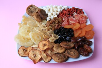 Plate with different dried fruits on violet background