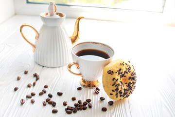 white porcelain teapot and cup with tea on a white wooden table on windowsill on sunny day